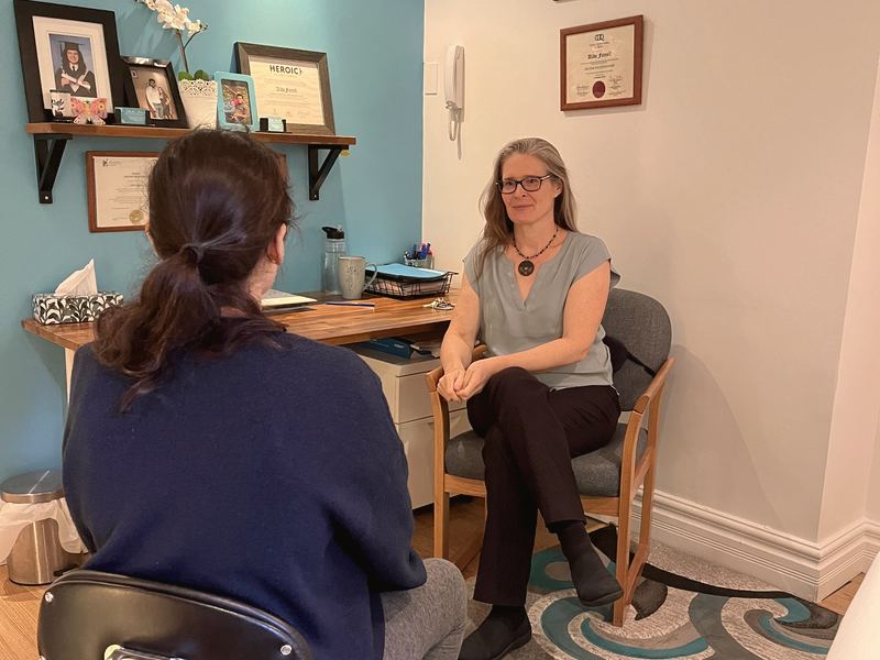 Alida Farrell, assise dans son bureau au mur turquoise, qui écoute une personne assise devant elle