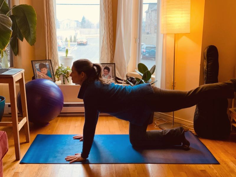 Alida en quadrupédie sur un tapis bleu, une jambe tendue, devant une grande fenêtre