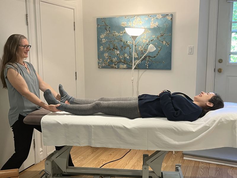 Alida Farrell tient les pieds d'une personne allongée sur la table de traitement, une toile d'amandier en fleurs au mur