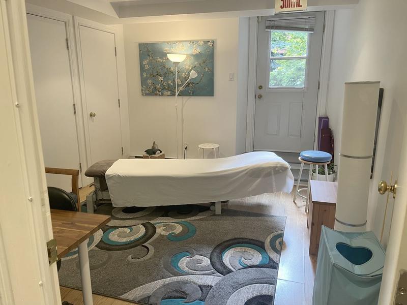 Une salle de traitement claire, la table, une toile au mur et la porte vitrée sur la verdure