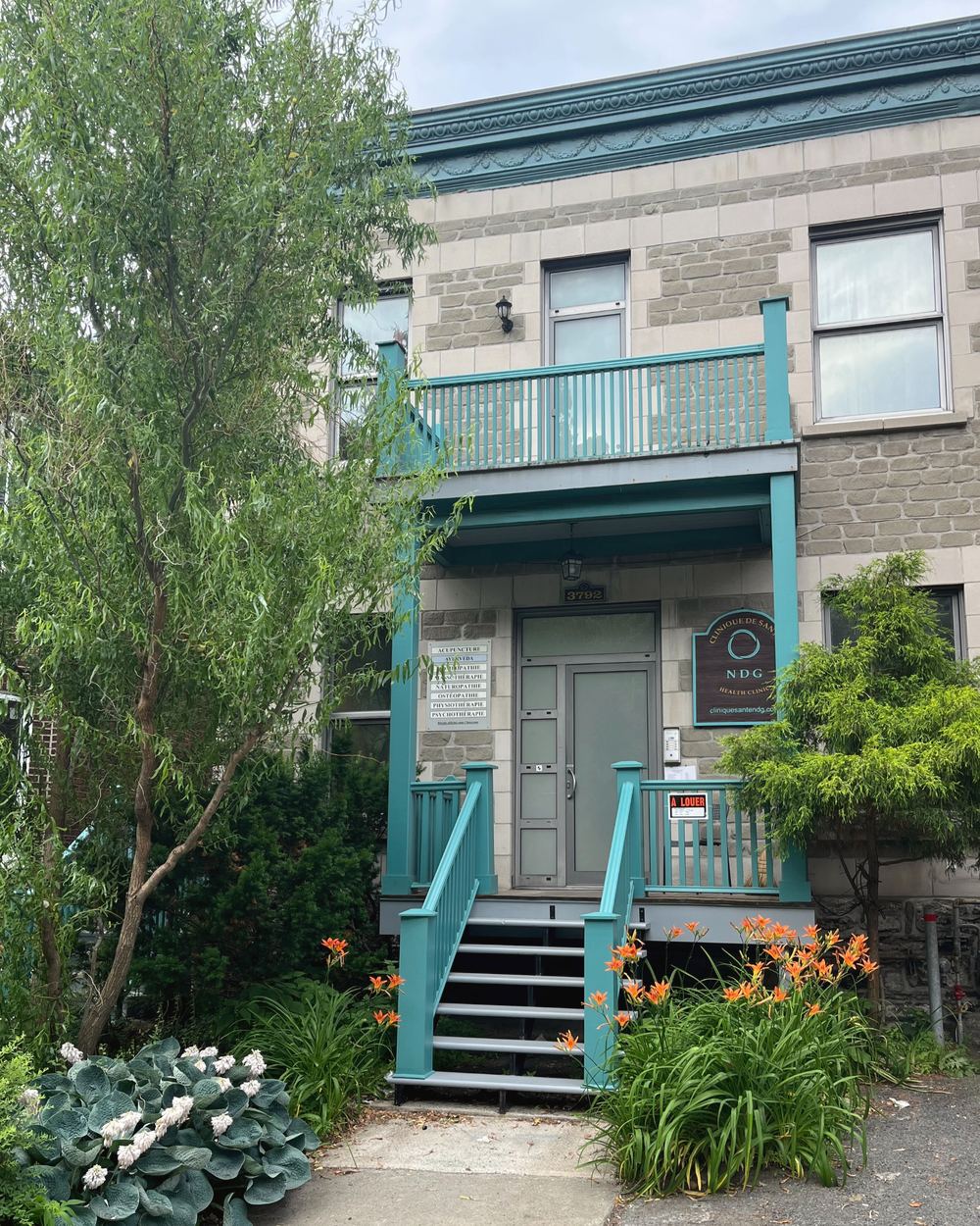 The front of the NDG Health Clinic, grey stone and turquoise stairs in the greenery