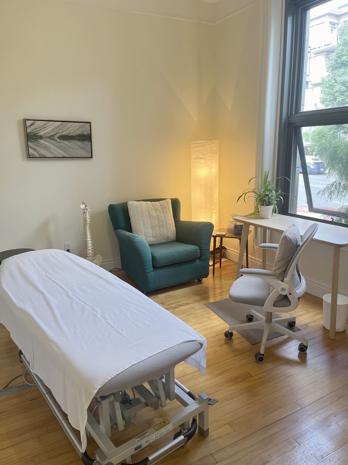 A bright treatment room, a green armchair, a paper lamp, a white desk and a large window onto the street